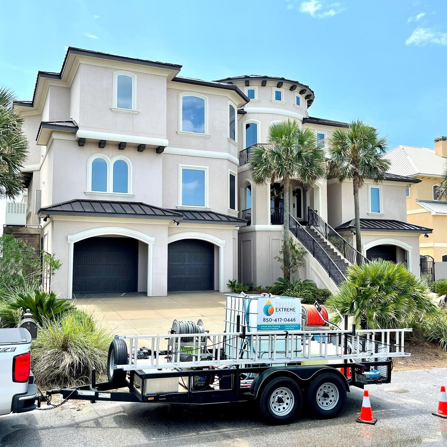 A two-story stucco house being cleaned. Pressure washing trailer parked in front.