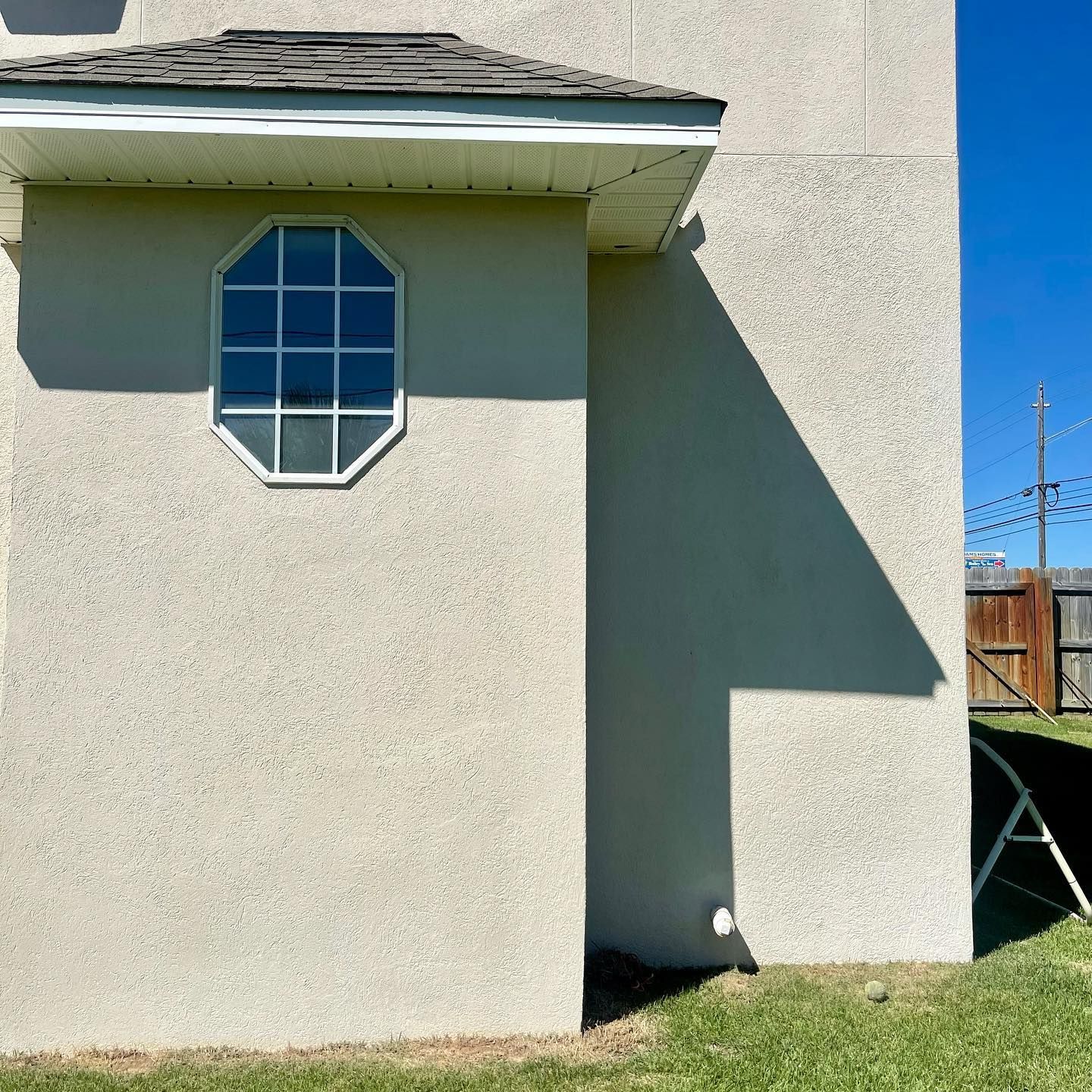 Beige stucco house with an octagonal window and a shadow on the wall.