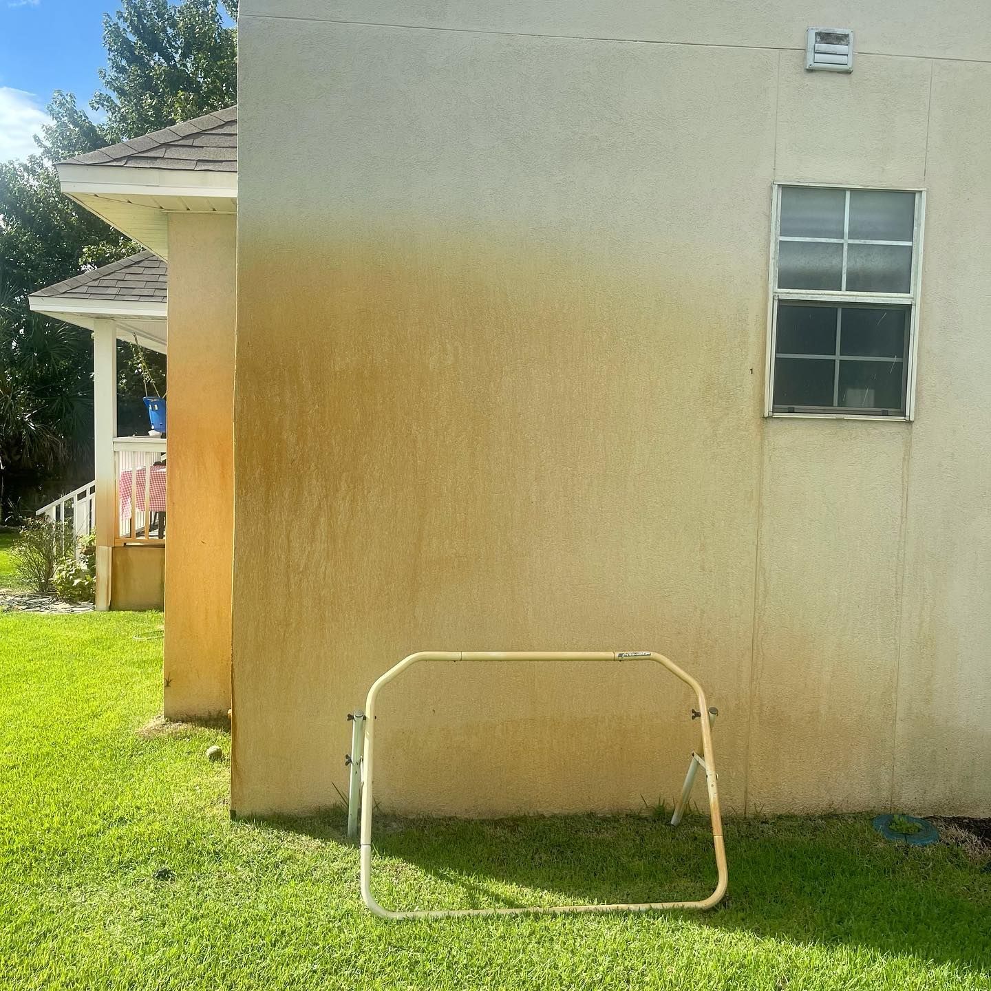 Yellow house exterior with discoloration; small window, folded metal frame, and green lawn.