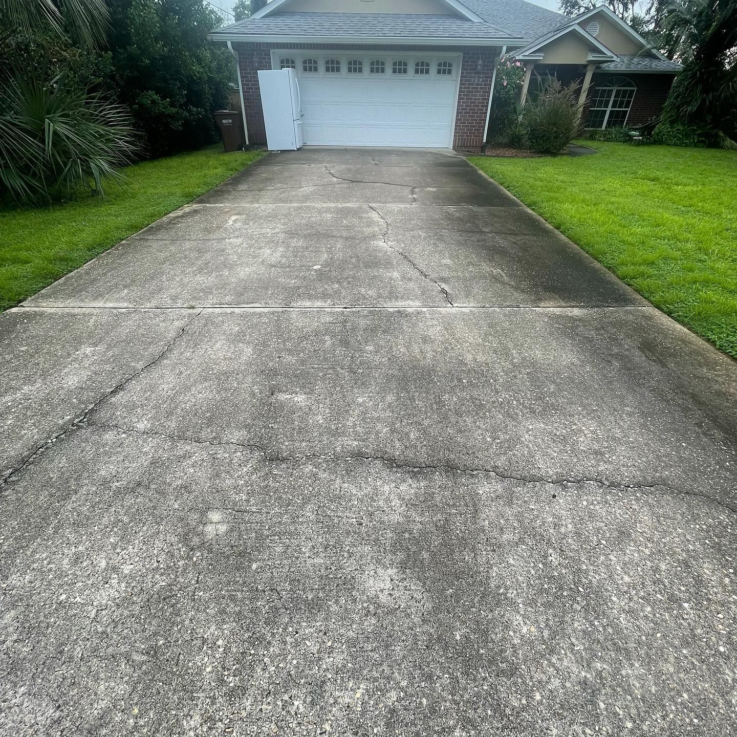 Driveway leading to a house with a closed garage door; cracked concrete, grass on either side.