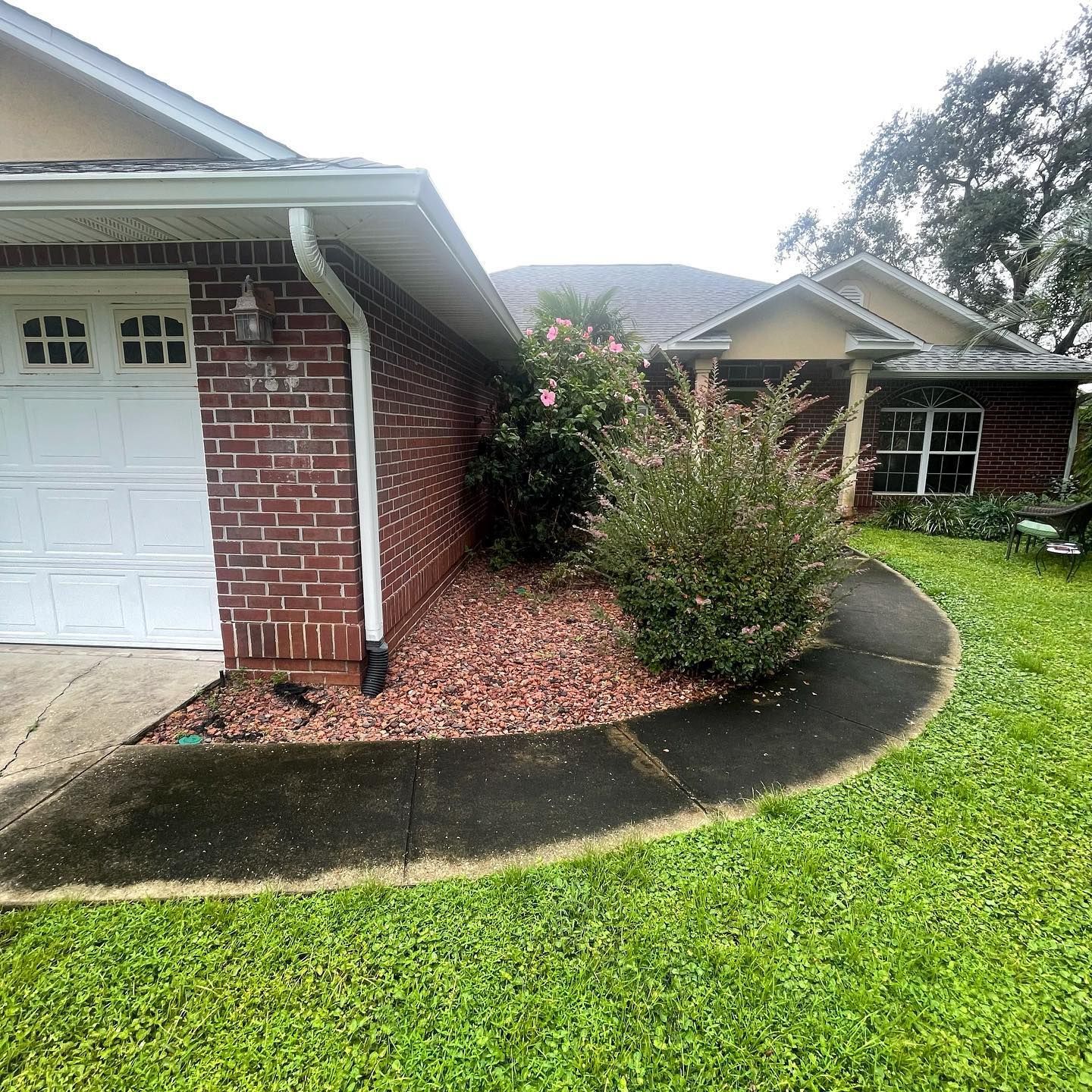 A brick house with a white garage door, garden bed, and a green lawn.
