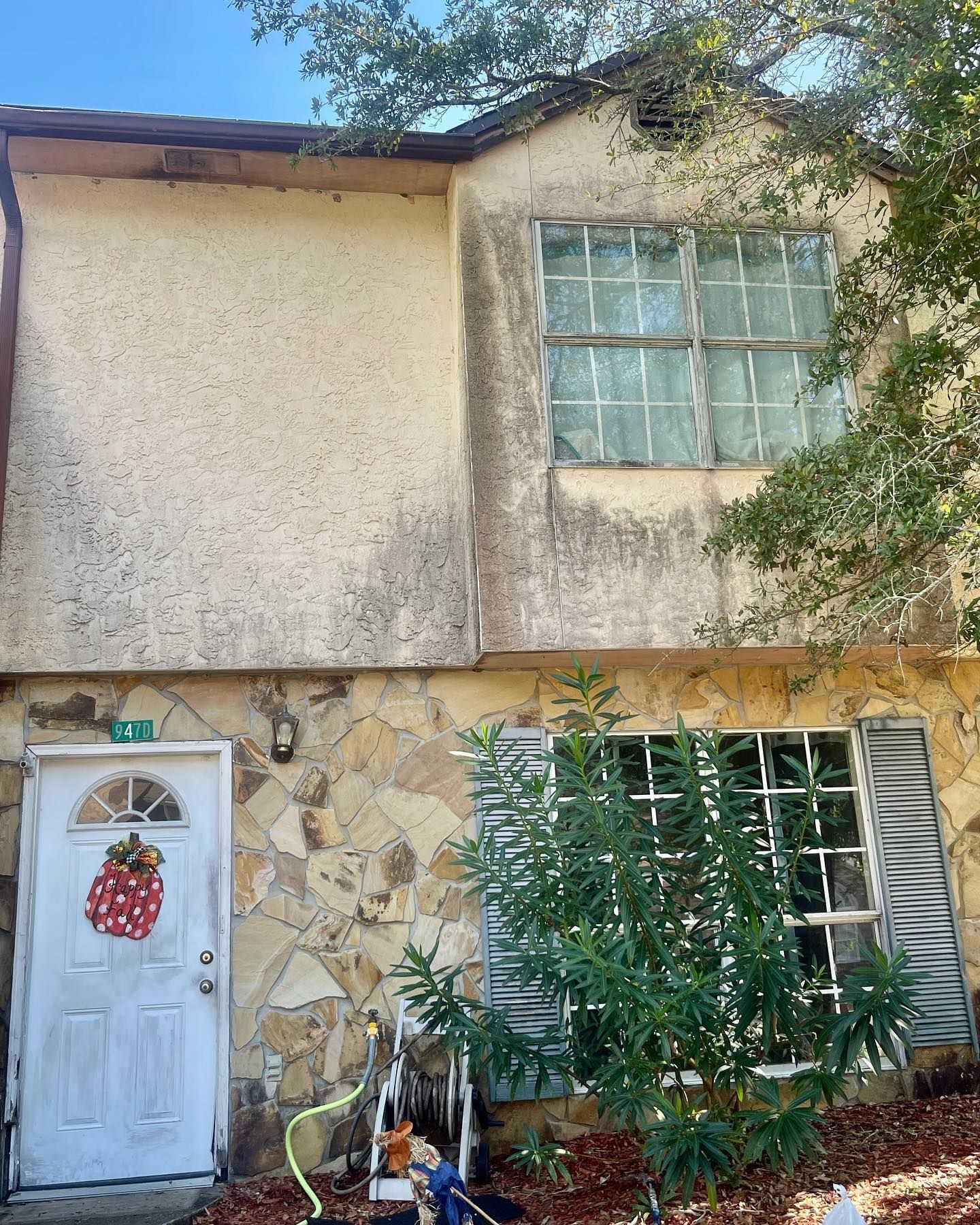 Two-story house with stained exterior; white door with wreath, stone and stucco facade, barred windows.