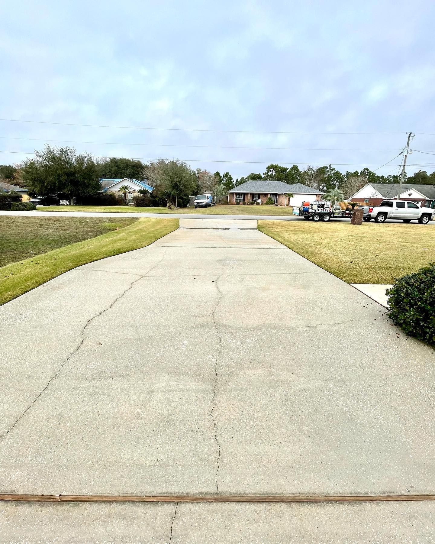 A cracked concrete driveway leads to a residential street under a cloudy sky.