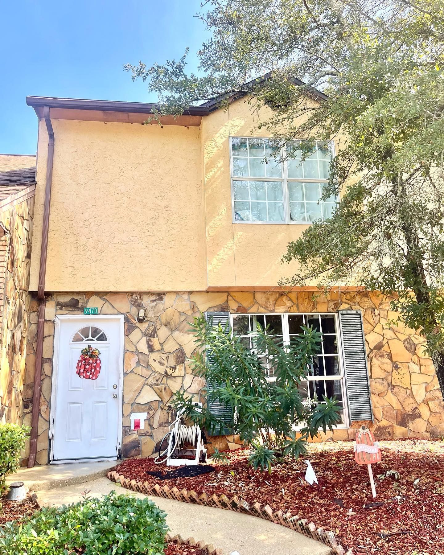 Two-story townhome with tan stucco and stone facade, white door with wreath, and small front yard.