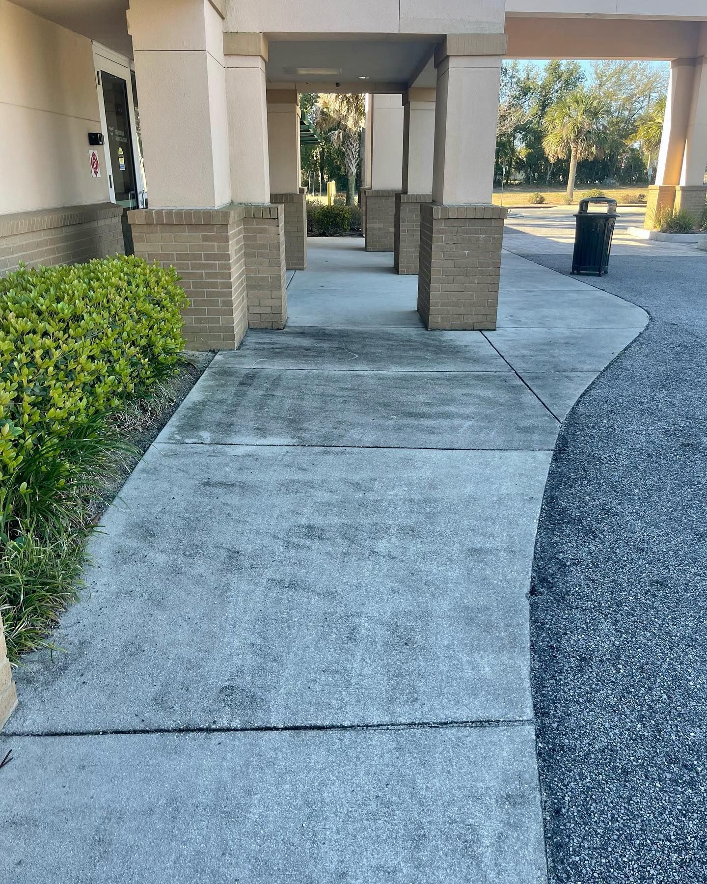 A concrete walkway with columns, leading to a building entrance. A trash can is visible.