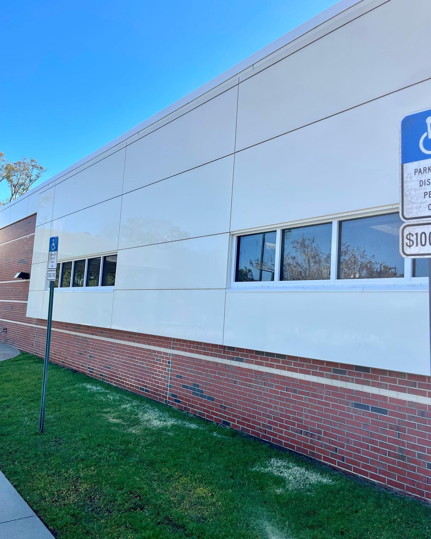 Building exterior with white siding above brick, accessible parking sign on right.