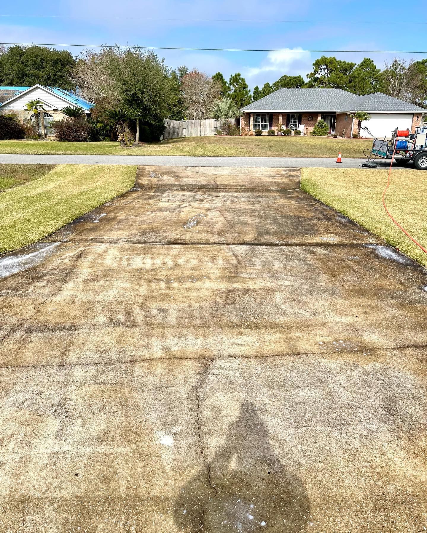 Concrete driveway with water runoff. Green grass borders the driveway. Houses and blue sky in the background.