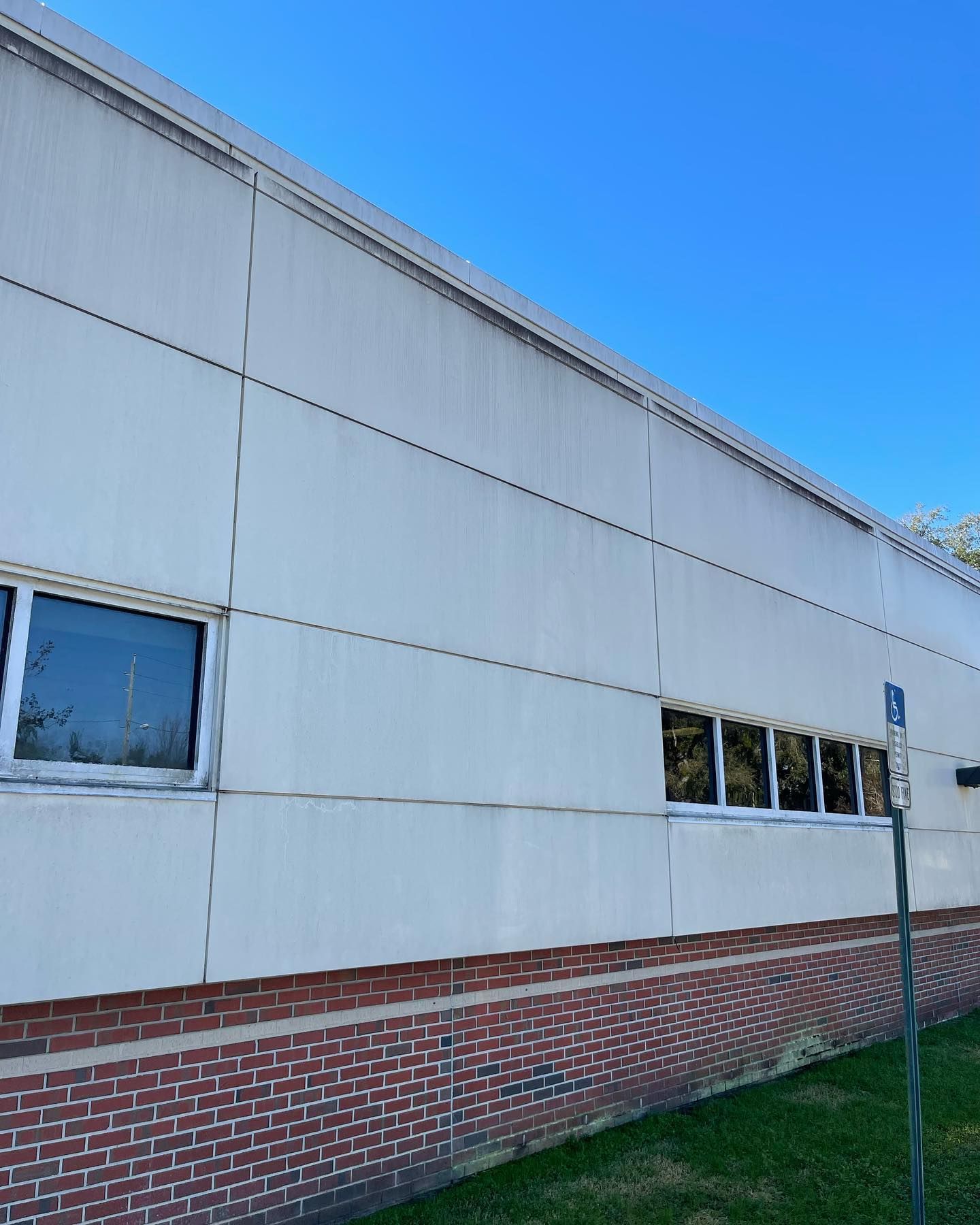 Exterior of a building with white panels, a brick base, and windows against a clear blue sky.