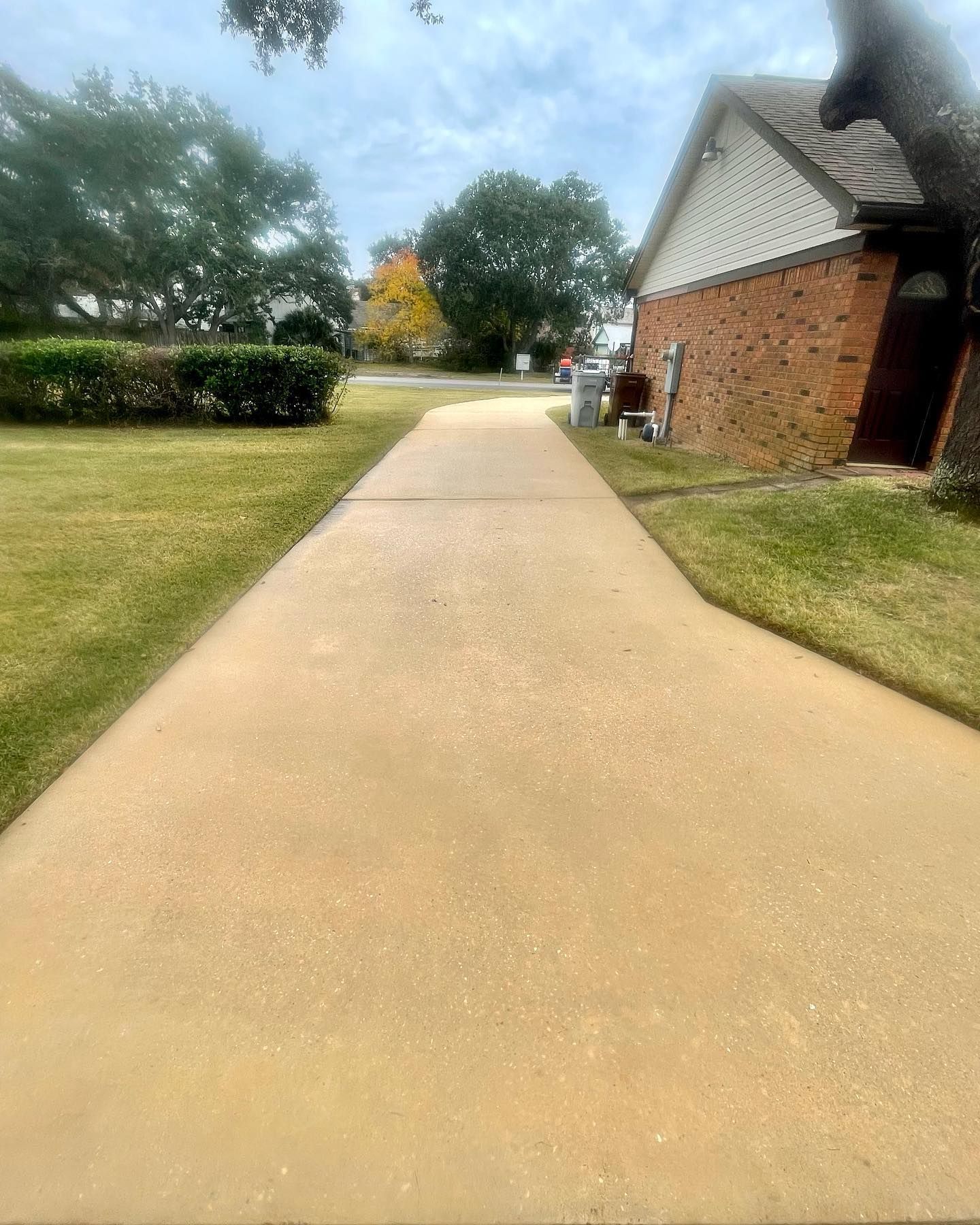Long, tan concrete driveway leading to a brick house on a cloudy day.