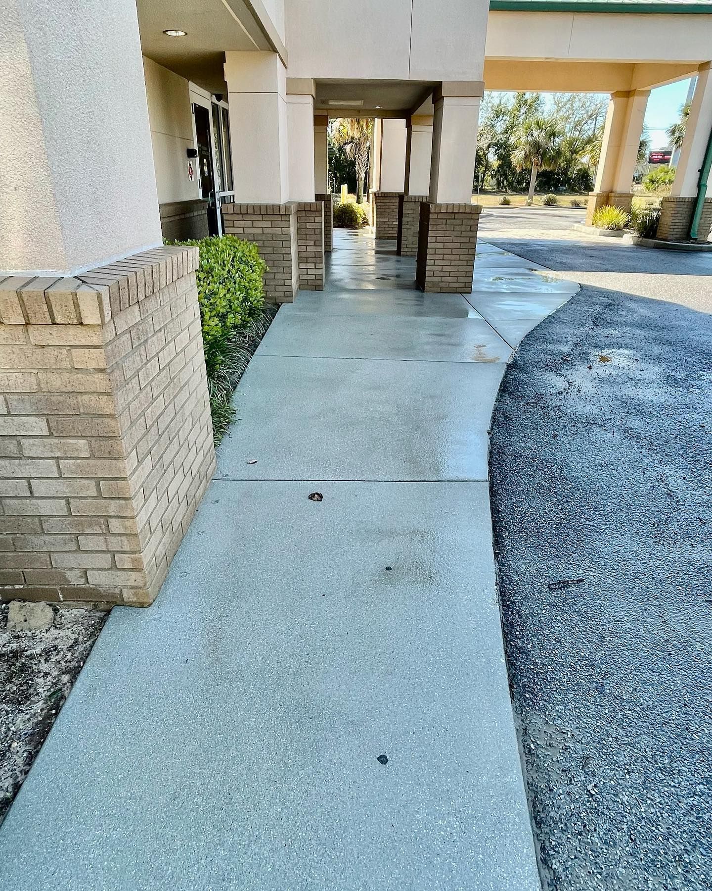 Exterior concrete walkway leading to a building entrance with beige columns and brick accents.