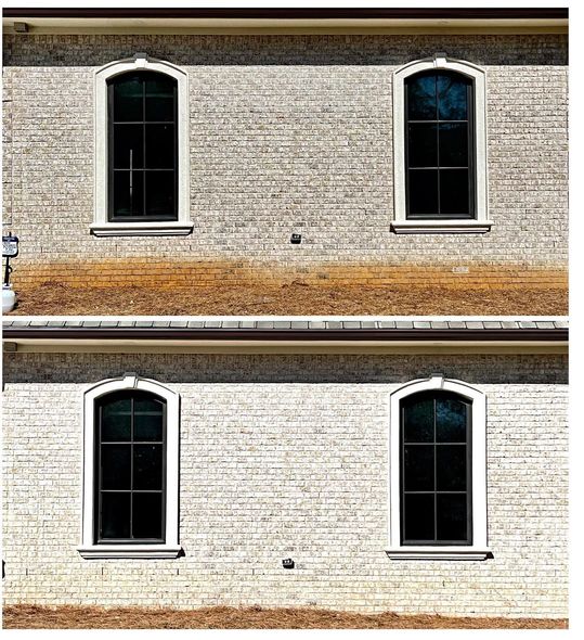 Four arched black-framed windows on a light brick wall, two above two, with a brown stripe of building between them.