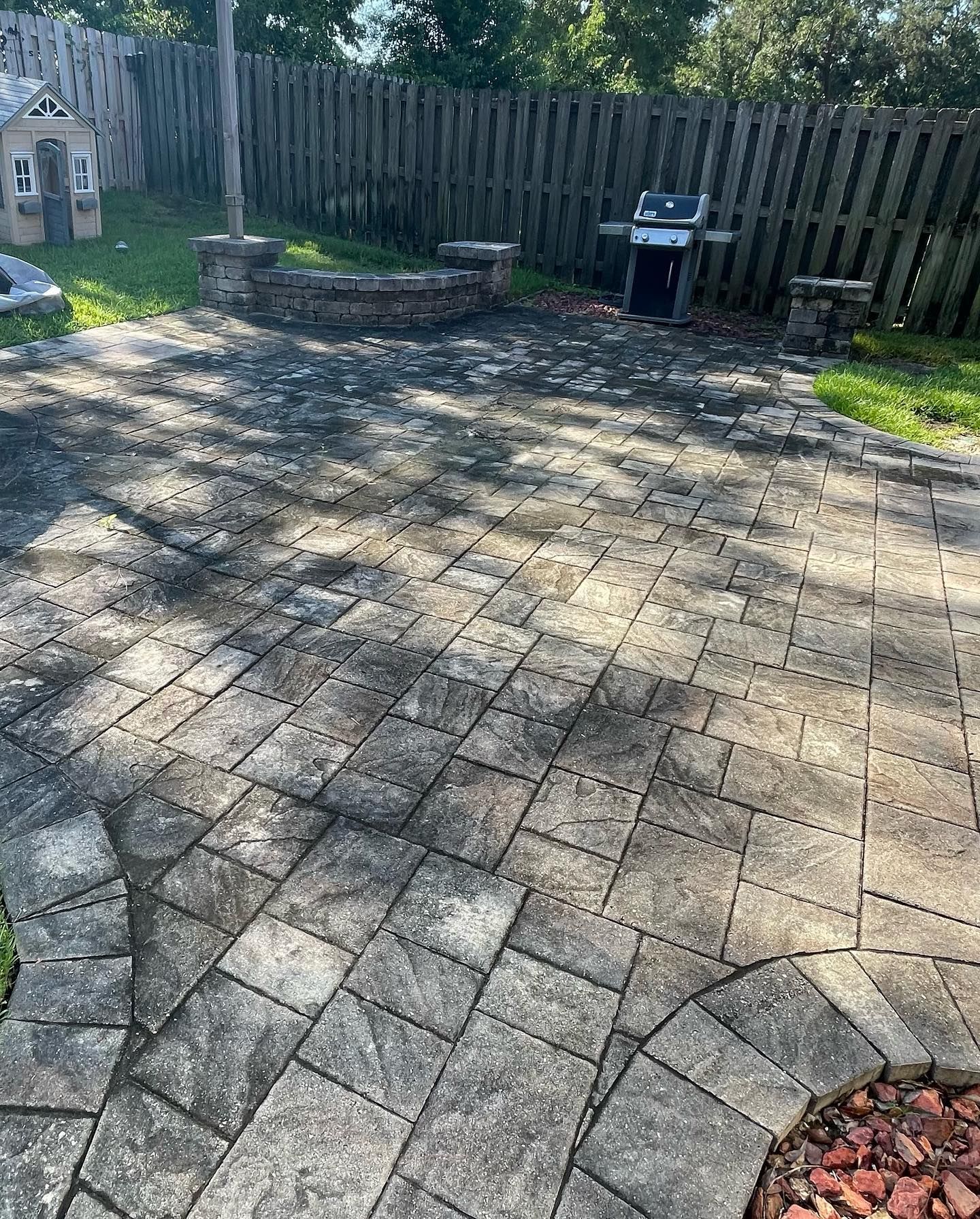 Patio with gray pavers, a fire pit, grill, and wooden fence.