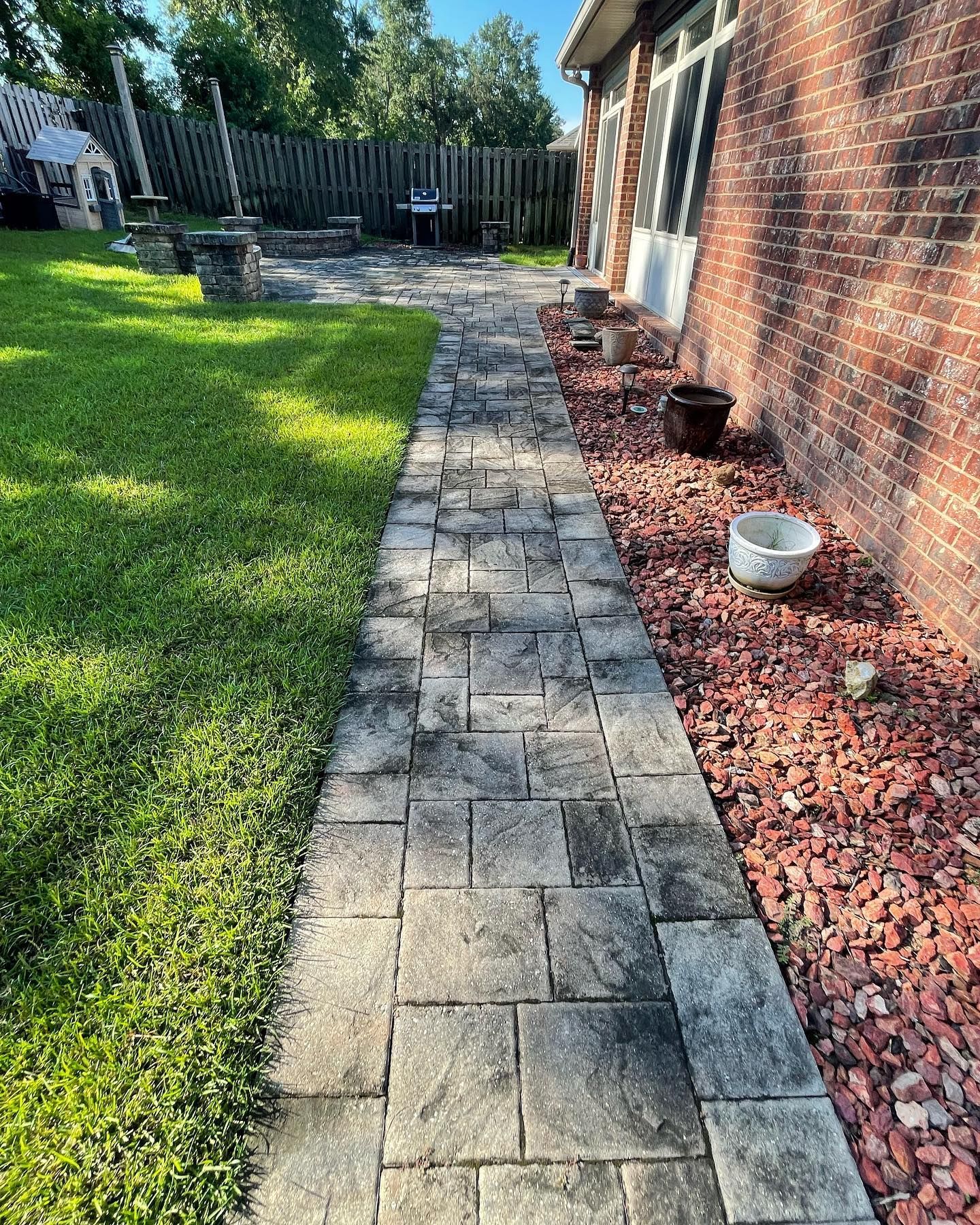 Brick pathway alongside a red brick building, bordered by grass and red gravel.