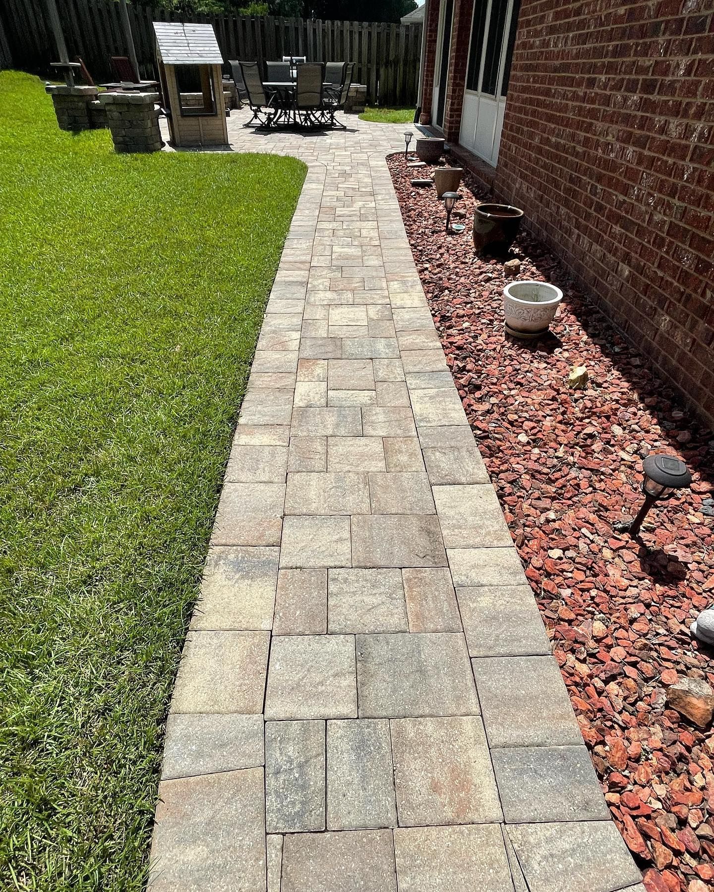 Stone pathway through a yard, bordered by green grass and red gravel, leading to patio furniture.