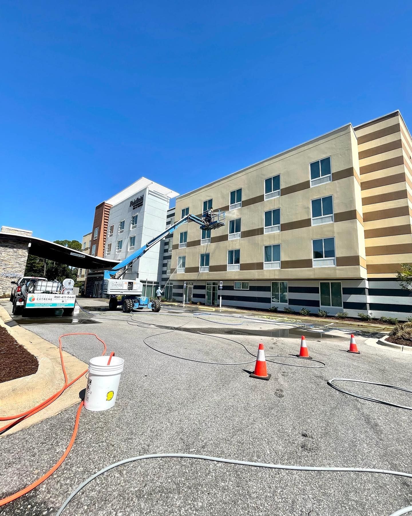 Hotel exterior under renovation with lift. Workers on a lift cleaning building facade. Blue sky overhead.