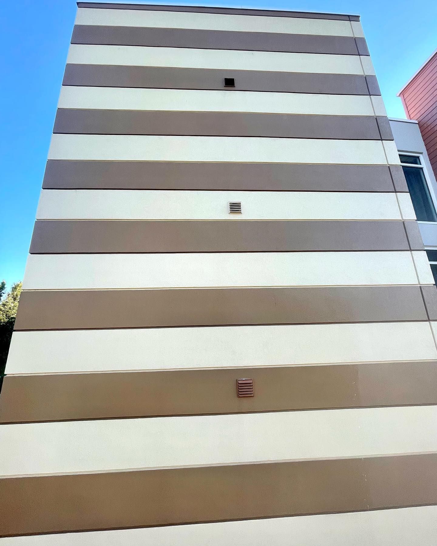 Tall building with alternating horizontal bands of beige and light brown against a blue sky.