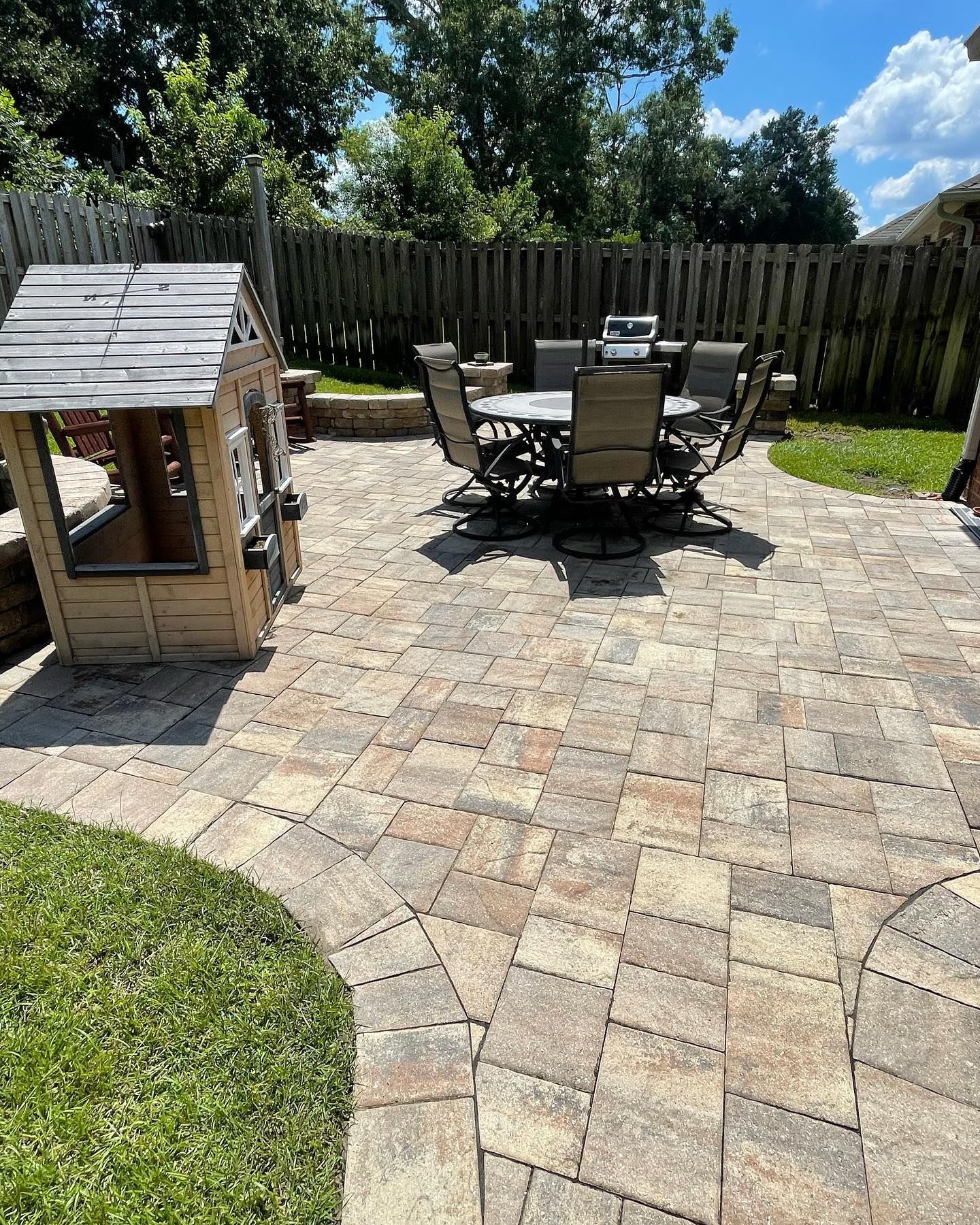 Paver patio with outdoor dining set and playhouse in a backyard.