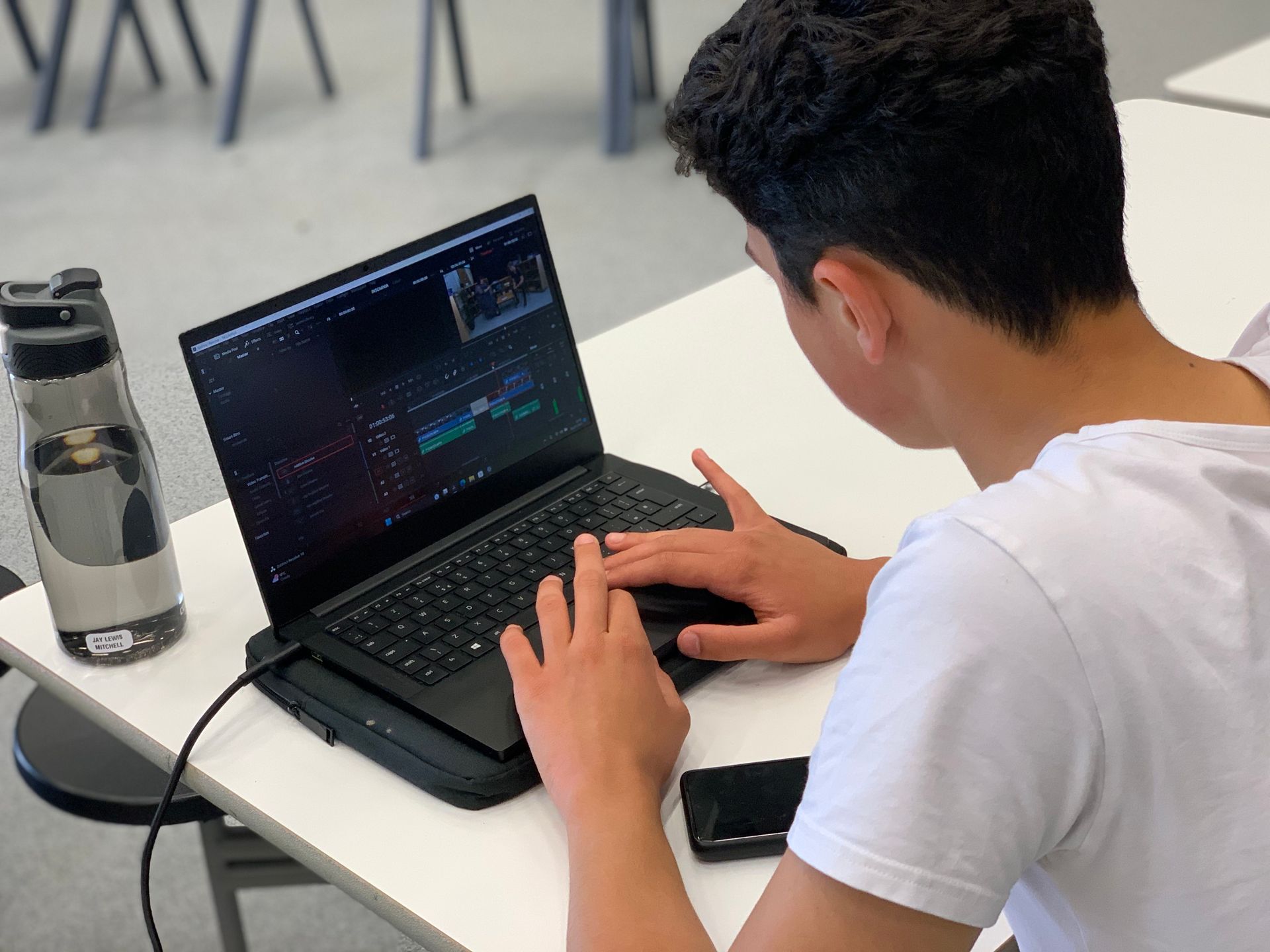 A young man is sitting at a table using a laptop computer.