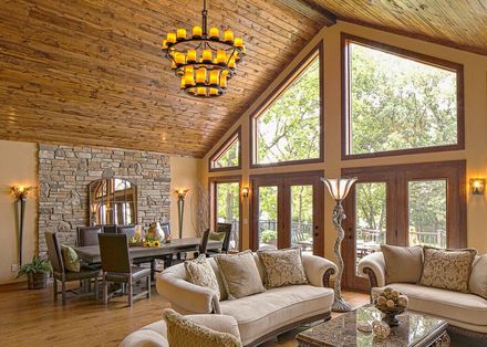 Rustic luxury living room with high wood ceiling, stone walls, large windows, and beige sofas