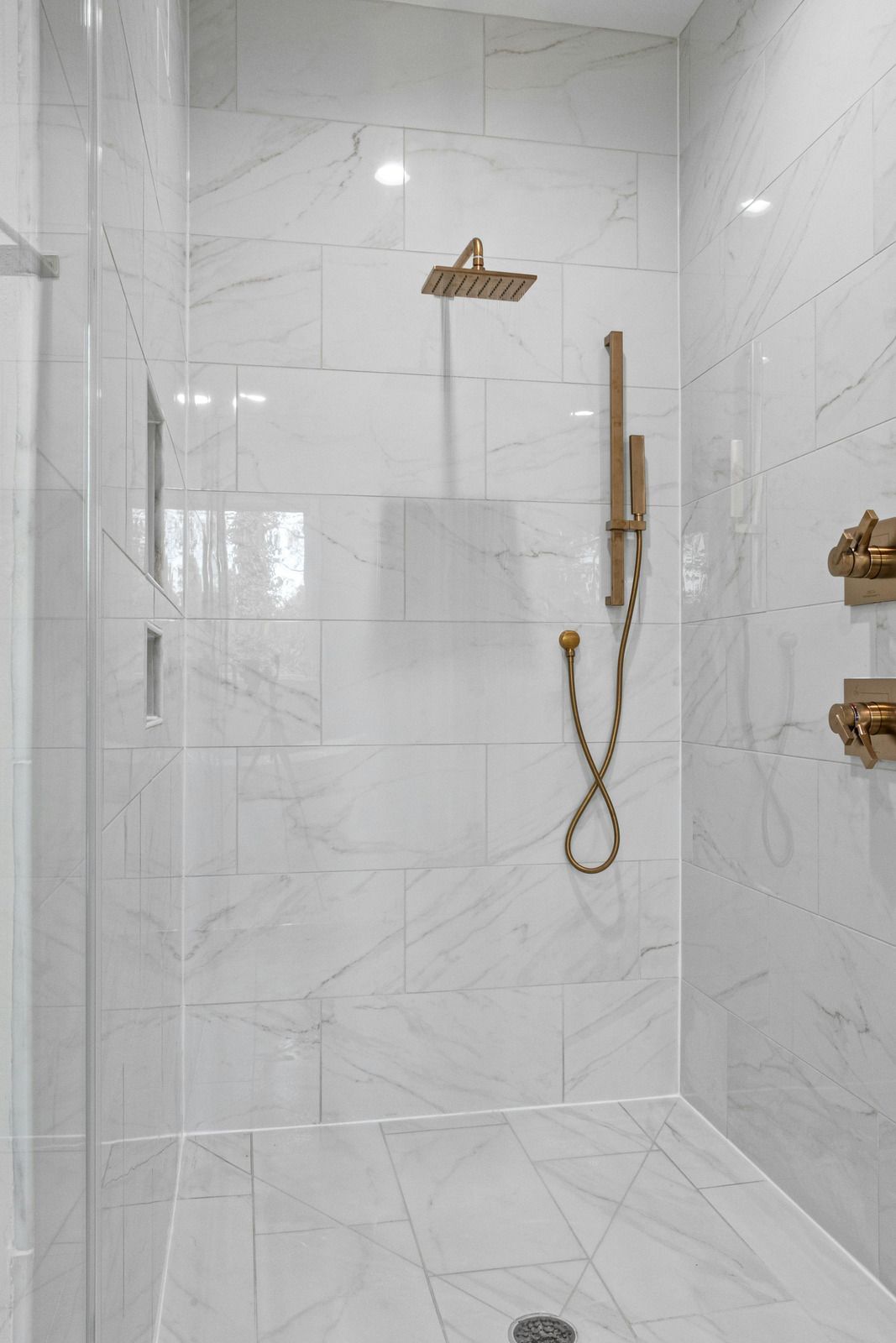 Modern white-tiled walk-in shower with brass fixtures and handheld showerhead