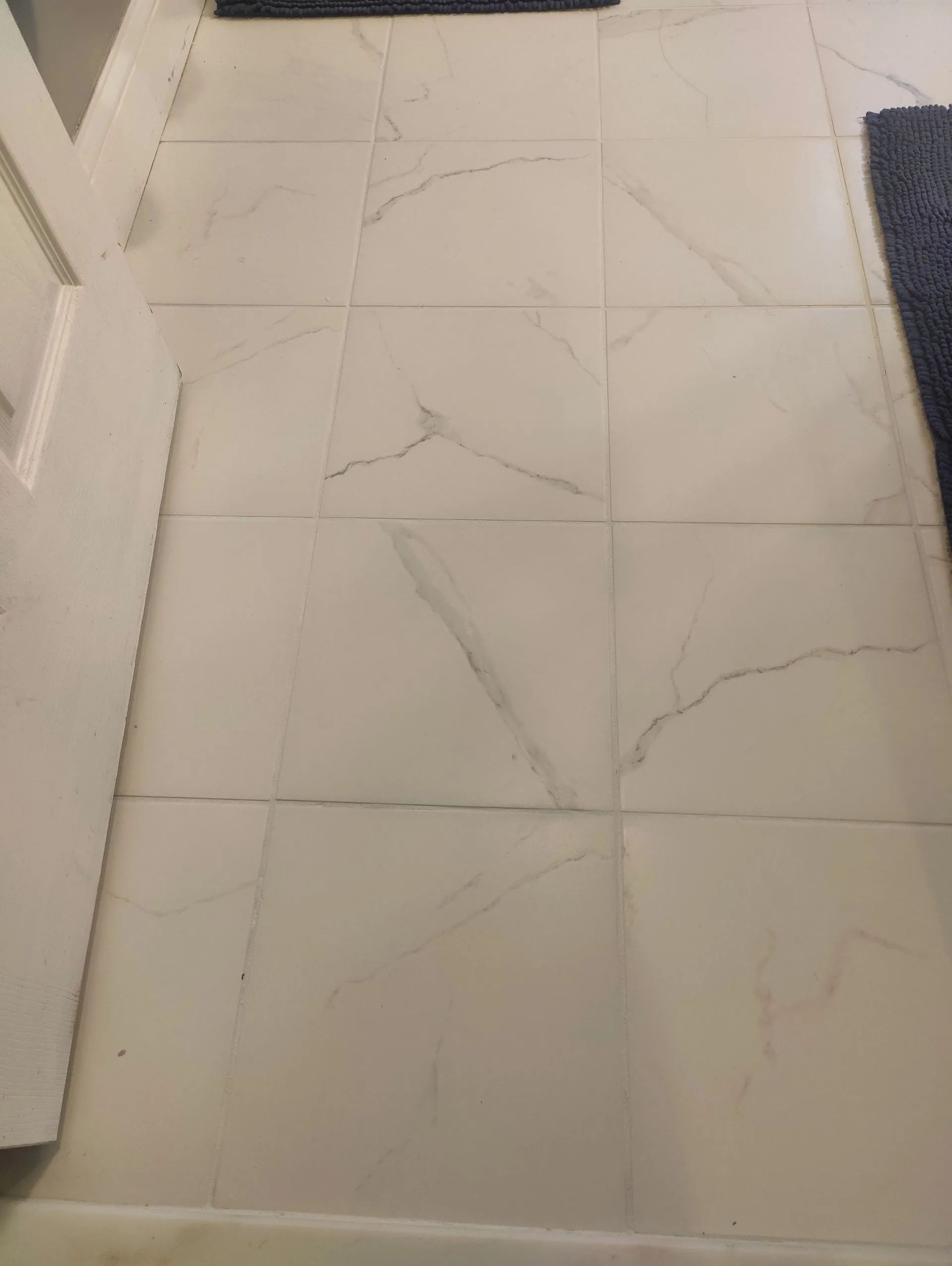 White tiled floor with gray veining and visible cracks between tiles near a doorway.