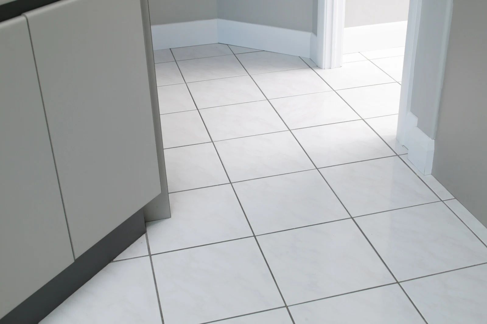 White tiled hallway and doorway with light gray cabinets on the left, seen from floor level