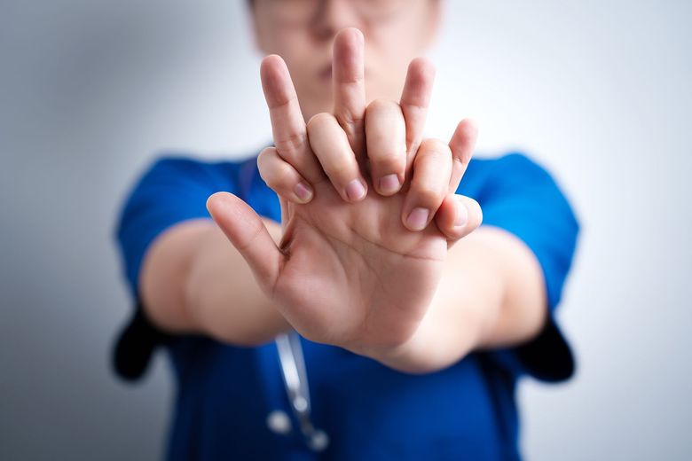 Doctor in blue scrubs holding both hands out in a stop gesture against a blurred background