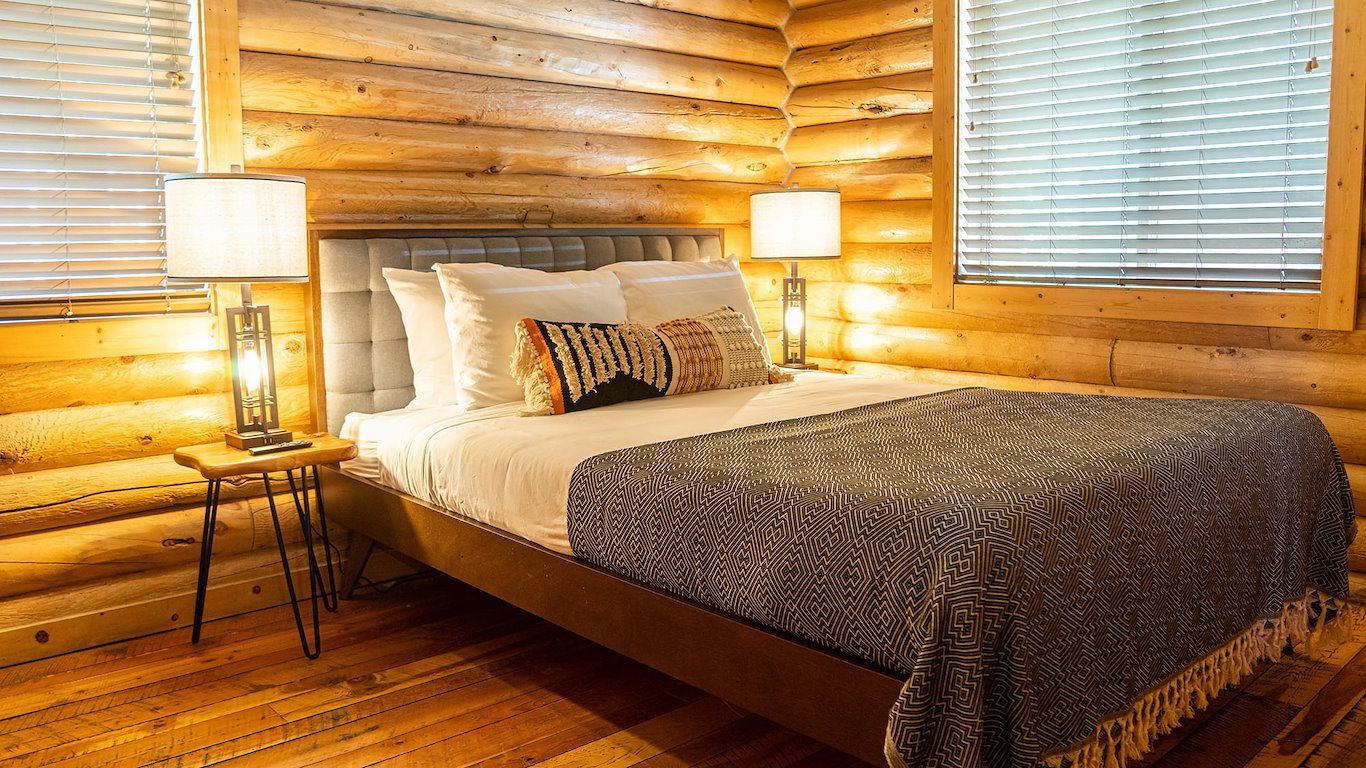 Bedroom with wooden walls, bed with patterned blanket, side tables with lamps, and window.