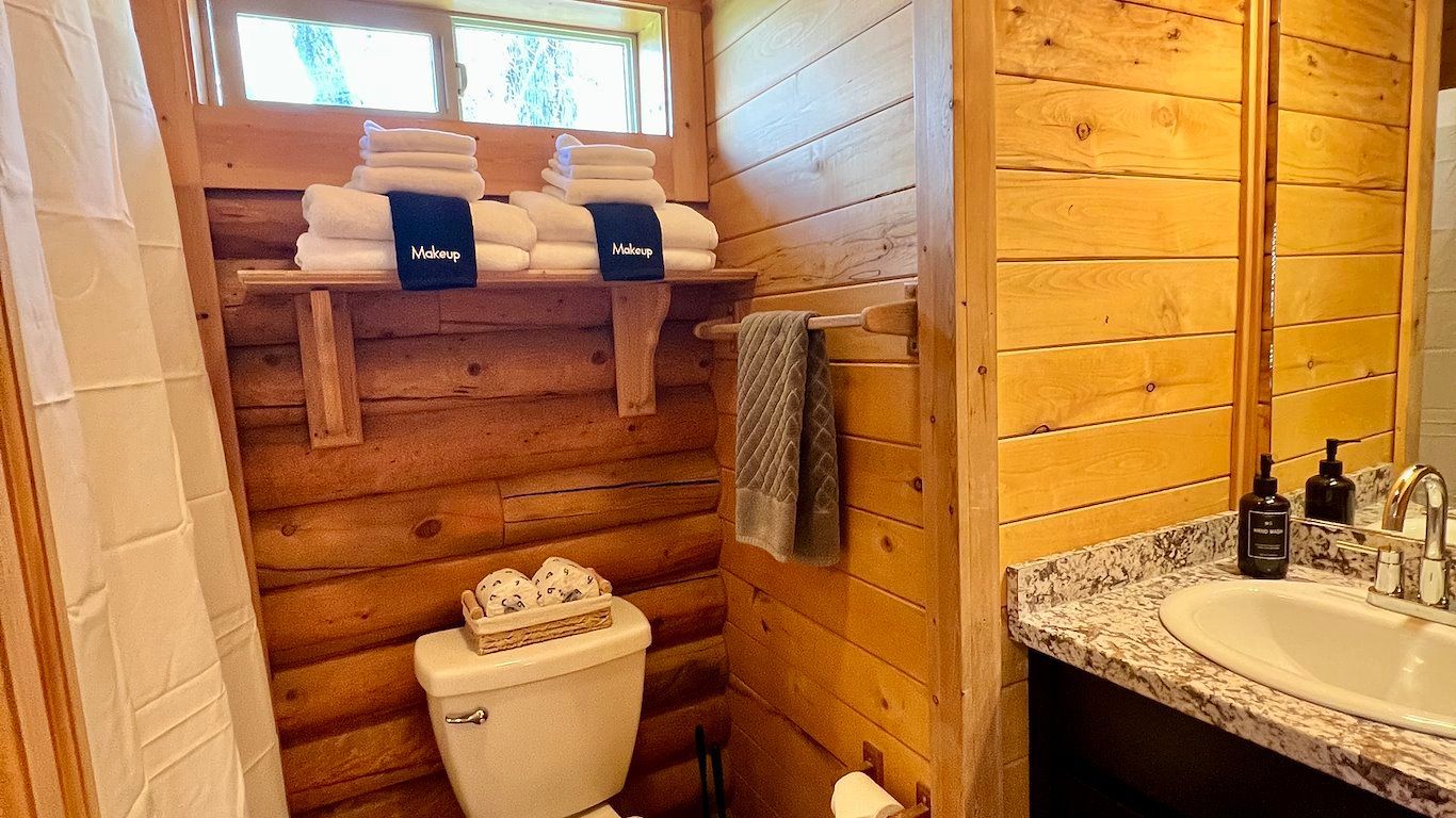 Cozy wooden bathroom with towels on a shelf, toilet, sink with a granite countertop, and window.