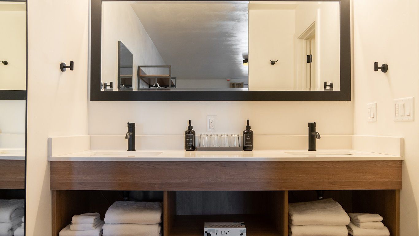 Bathroom with double sinks, a large mirror, and open shelving displaying towels.