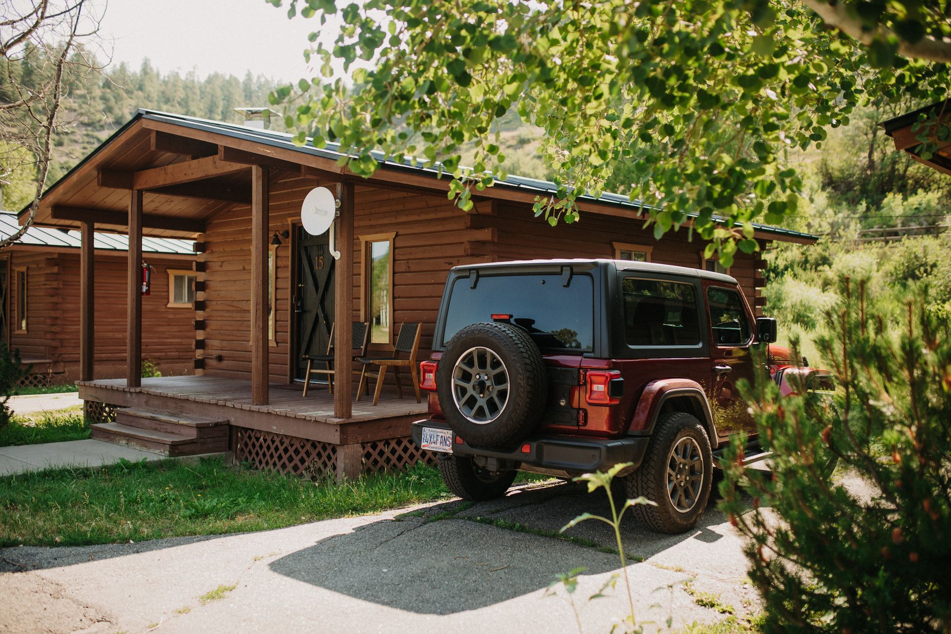 Red Jeep parked near a log cabin with a porch in a wooded area.