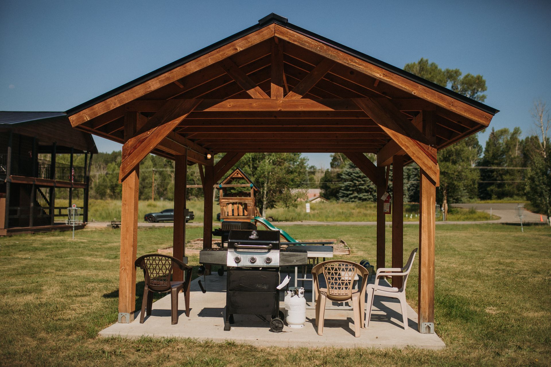 Wooden gazebo with a grill and seating in a grassy area.