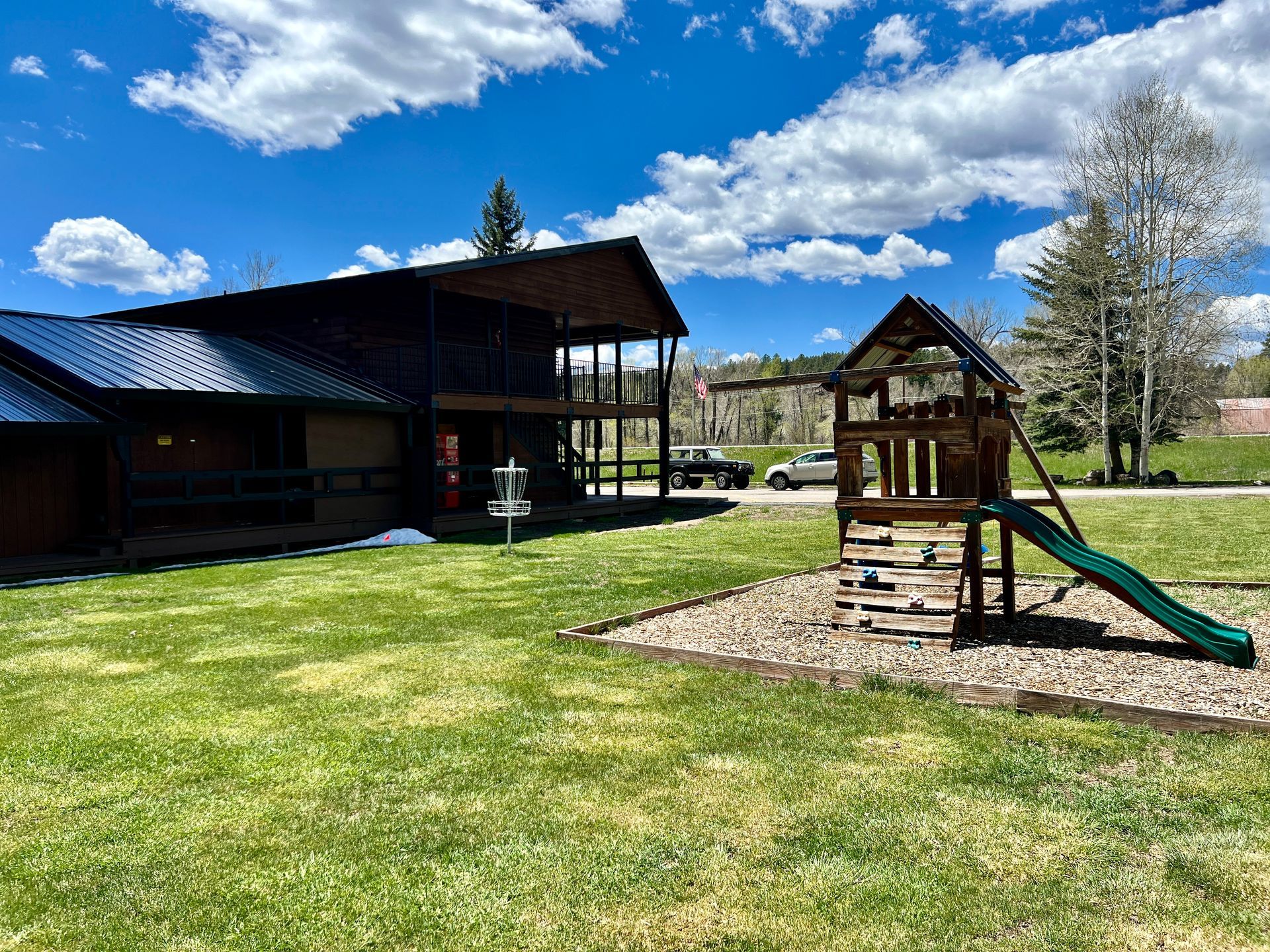 Building with a playground on a grassy field under a blue sky with clouds.