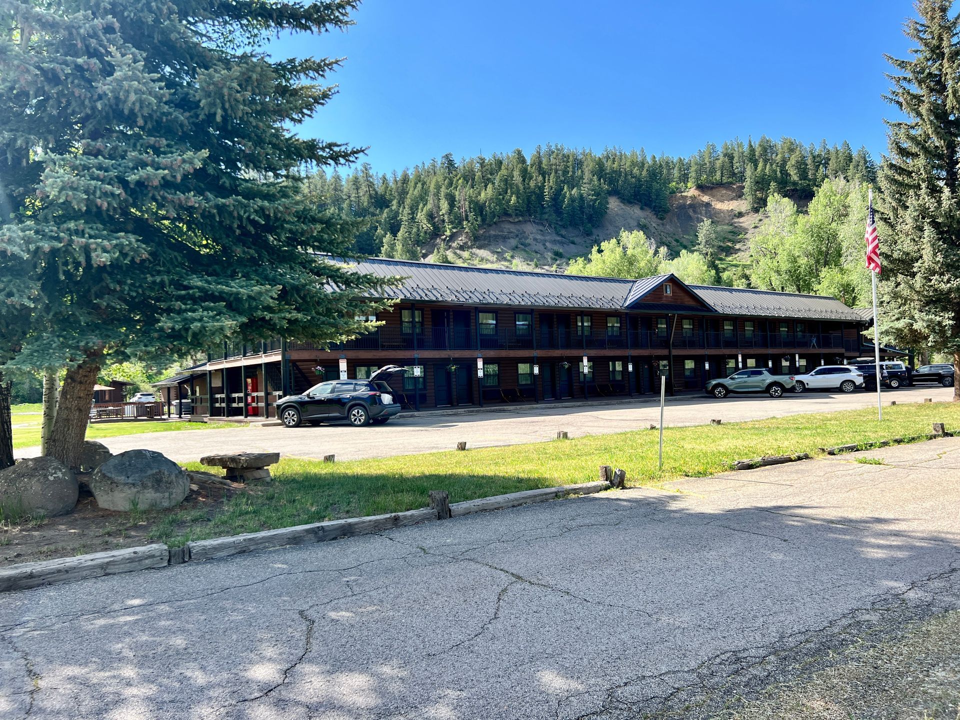 A long, wooden motel building in a mountainous setting with cars parked outside.