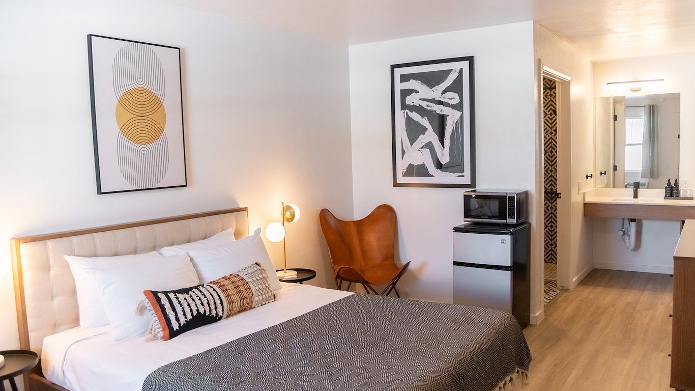 Hotel room with a bed, art, a butterfly chair, a microwave and mini fridge, and a bathroom.