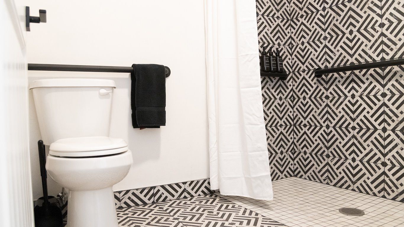 Black and white bathroom with geometric tile, a toilet, shower with white curtain and a towel rack.