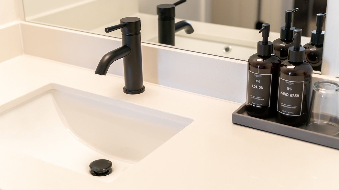 Bathroom sink with black faucet, white countertop, toiletries in brown bottles.