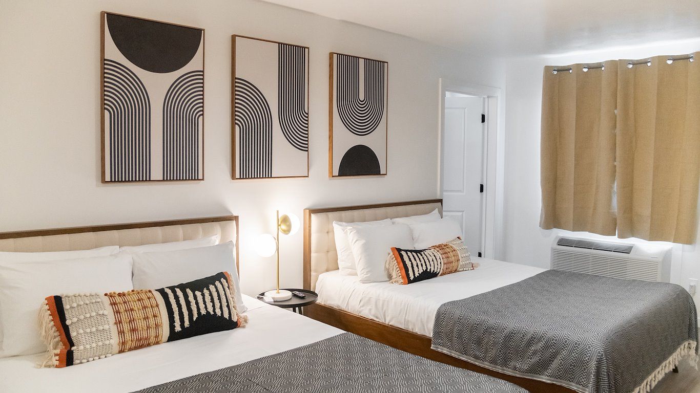 Bedroom with two beds, modern art on the wall, neutral tones, and a window with curtains.