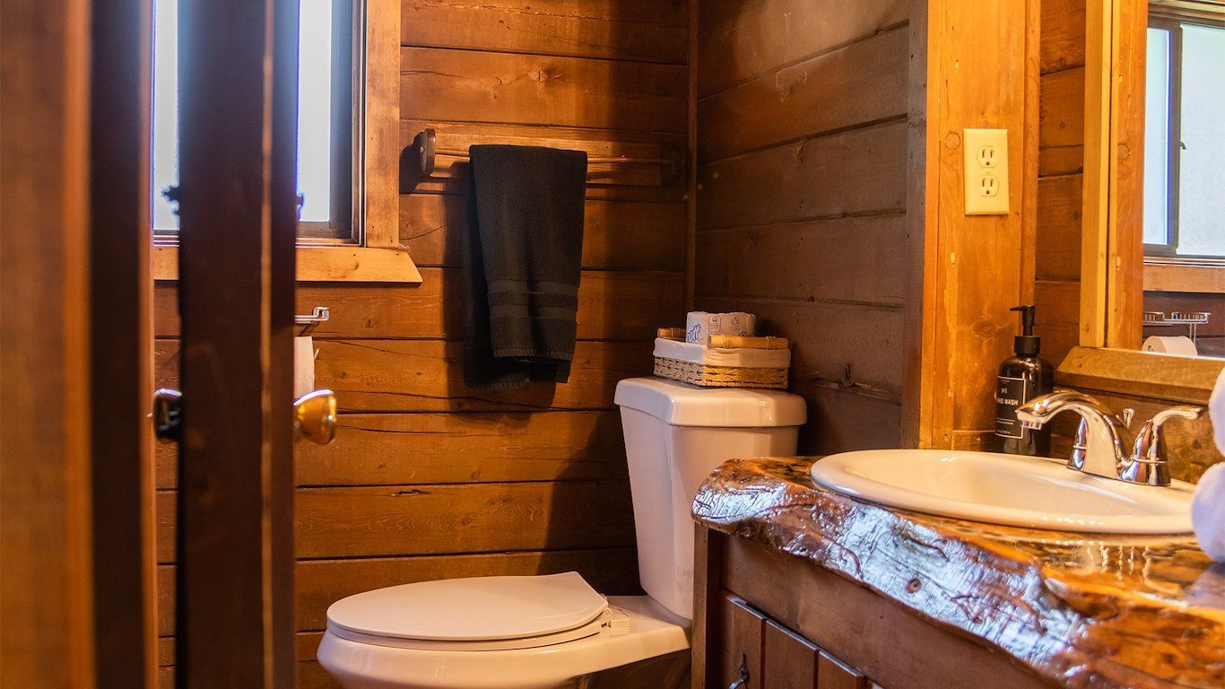 Rustic wood-paneled bathroom with toilet, sink, towels, and a small window.