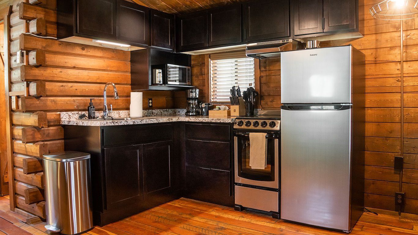 Small rustic kitchen with stainless steel appliances and dark cabinets, set in a cabin with wood paneling.
