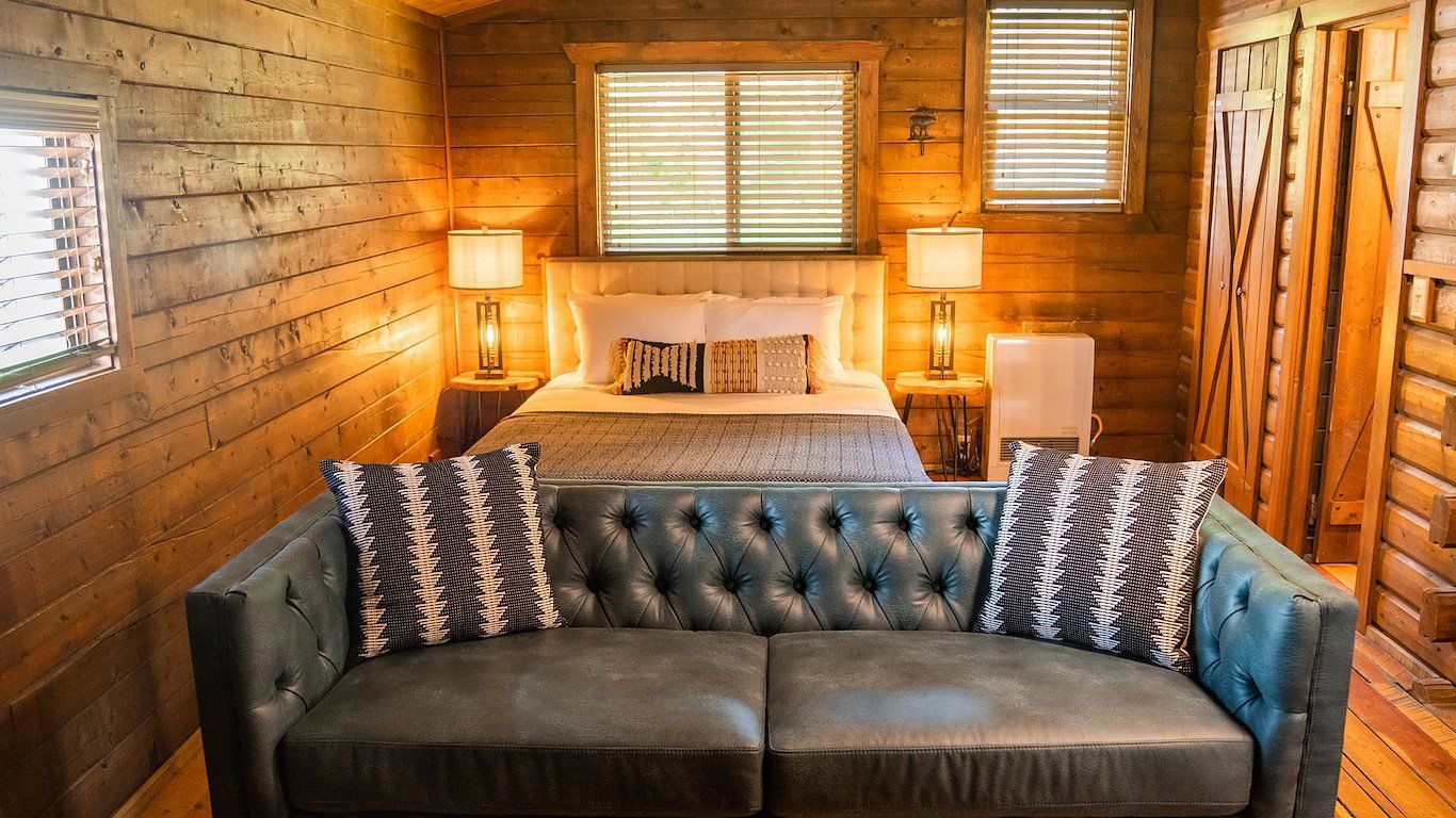Cozy bedroom with a blue sofa, bed, wood walls, and warm lighting.