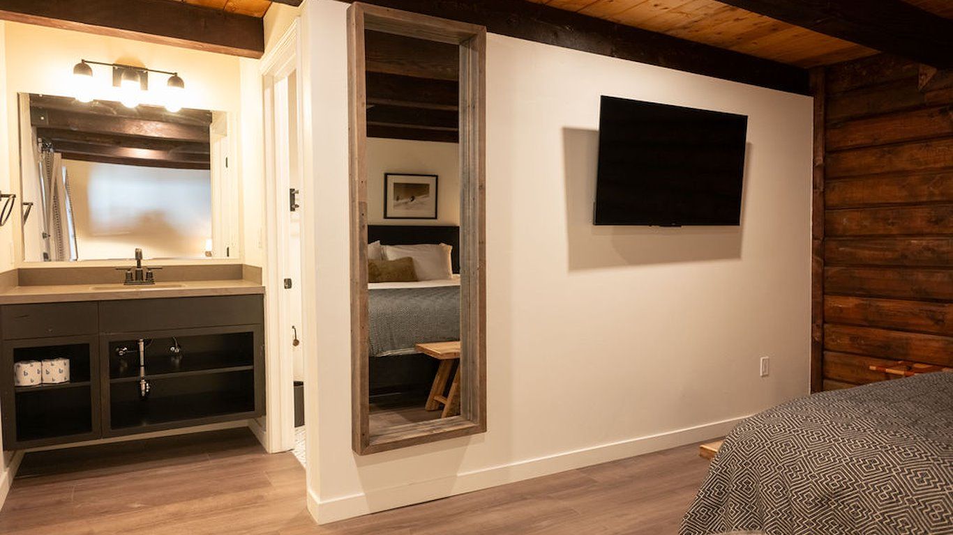 Bathroom with vanity, full-length mirror, and a TV on the wall next to a log-wood paneled wall.
