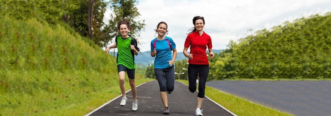 Three runners in colorful shirts jogging on a road beside lush green hills