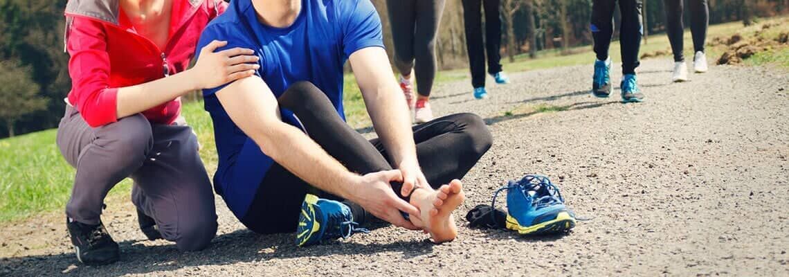 People tying a shoelace outdoors on a gravel path, with a blue shoe nearby