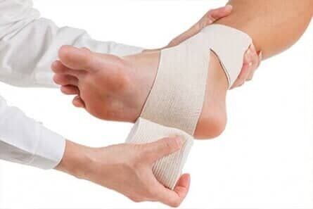 Hands wrapping a beige bandage around an ankle and foot