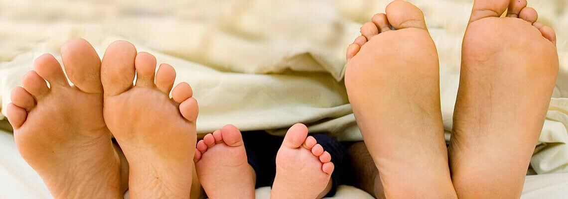 Three pairs of bare feet resting on a blanket, from smallest baby feet to larger adult feet.