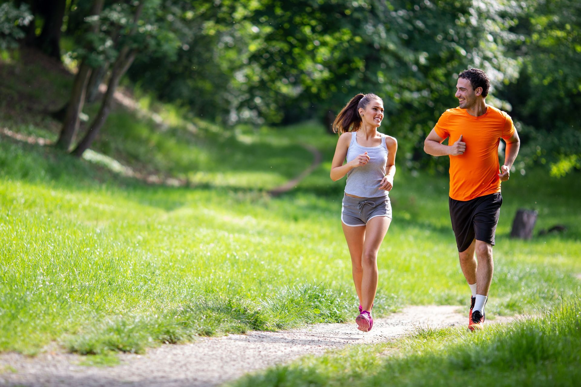 Two runners in orange and white workout clothes jogging on a sunlit park path