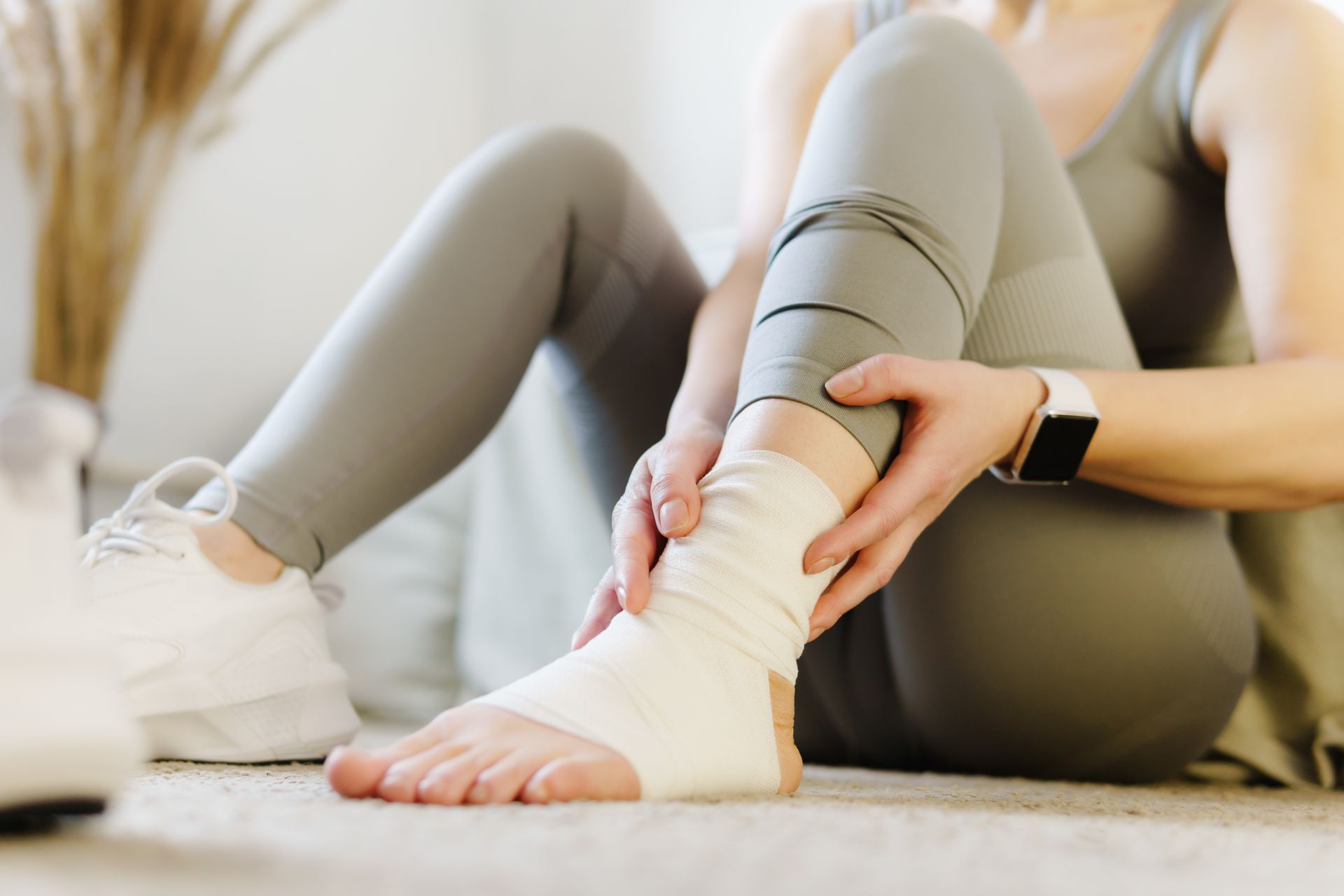 Person wrapping an ankle with a white bandage while seated on the floor
