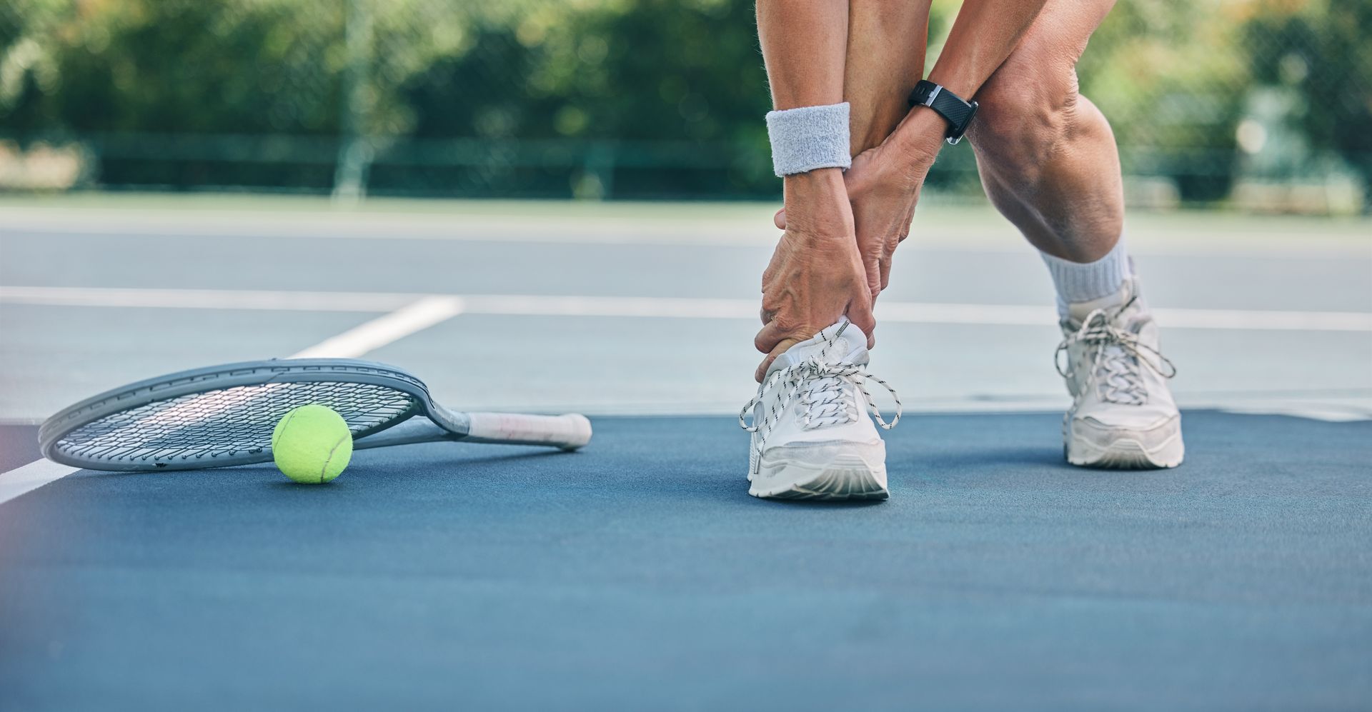 Tennis player bending to adjust shoelace beside racket and tennis ball on court