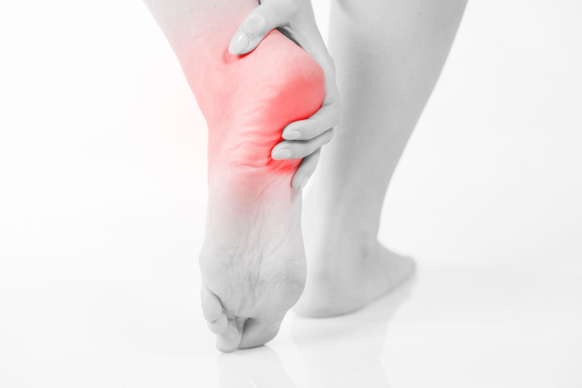 Person holding a painful, red-highlighted heel and ankle while standing on tiptoe